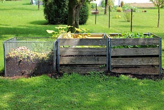 three wooden compost bins in a grassy yard