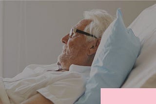 white haired man with glasses laying in hospital bed using FaceTime for Families program to communicate during Coronavirus