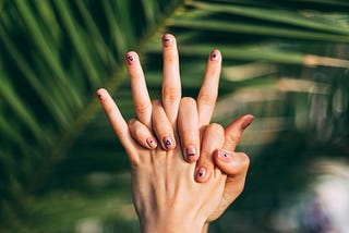 One hand holding the other in front of a palm tree leaf.
