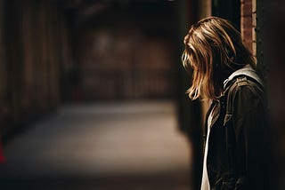 woman stood alone in an alley way looking sad with her head down