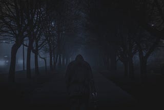 Dark figure heading down a dark lane lined with trees and carrying an unlit lantern