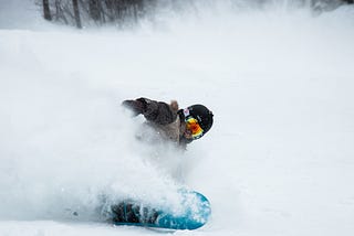 A snowboarder making a sharp cut on the mountain while kicking up snow.