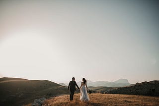A photograph of a bride and groom on a mountain, holding hands and looking into the distance