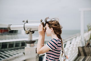 Young girl looks out to sea through binoculars on a pier