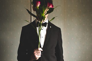 A man in a suit stands holding flowers up to his face.