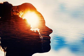 The silhouette of a woman’s face against a background of clouds. In her silhouette has an image of the rising sun behind clouds superimposed on it.