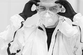 A man is wearing personal protective equipment. He is holding his eye goggles with gloved hands