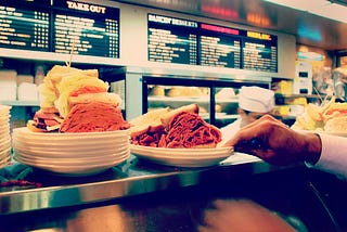 Two pastrami sandwiches stacked high on a deli counter.