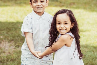 a picture of a boy and a girl standing on grass, they’re holding hands and are both smiling — 3 life lessons i learned by raising a disabled and a non-disabled child together — illumination — life — life lessons — parenting — challenge — growth — self-development — family — family life — kristin_schuhknecht — writemetothemoon.com