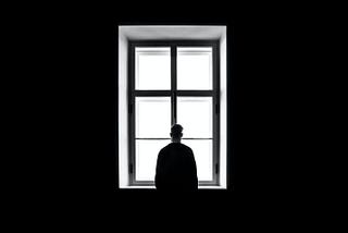 A man in a dark room stands in silhouette at a window