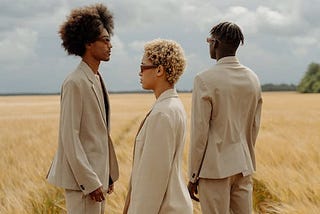 Three people standing on a rye field, all looking in different directions.