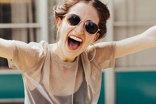 A young woman is dancing joyfully and smiling broadly into the camera. She looks as if she has had great news or some kind of wonderful success.