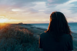 Woman alone gazing toward sunset over the beach
