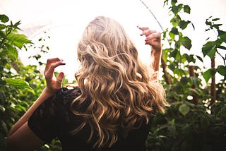 A woman with glossy blonde hair faces green foliage