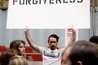 photo of man holding ‘forgiveness’ sign posted on mickey markoff air sea show exec 2022 post on forgiveness