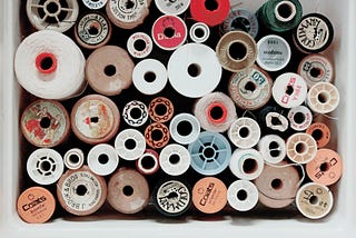 An upper view of a box full of spools of sewing thread. Gives of a colorful vintage vibe.