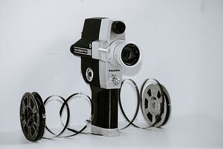An old Fujica movie camera, small and handheld, with two spools of movie film framing it on the left and the right