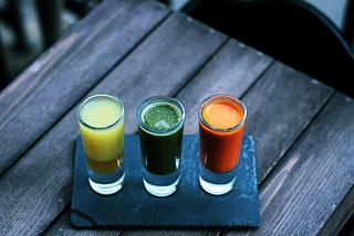 three glasses with healthy protein drinks, one yellow, one green and one orange