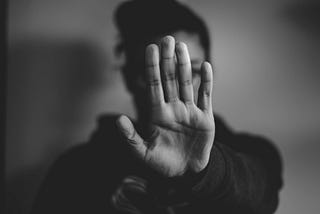 A black-and-white image of a person holding their arm stretched out in front of them, hand up to say ‘stop’.