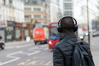 Person wearing a headset looking towards a traffic intersection. Buses and buildings are seen are in the background