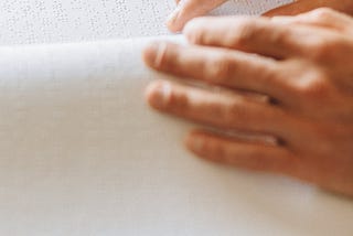 Hands scanning over a page embossed with braille.