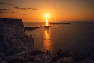 Sun setting into the sea people sitting on a rock watching , Spain