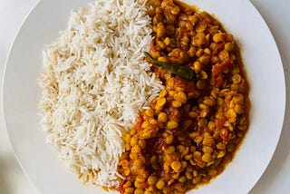 A plate half filled with white rice and the other half with lentils in a tomato sauce.