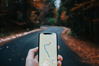 Phone screen showing a highlighted path on a navigation app. Tree-lined street in the background