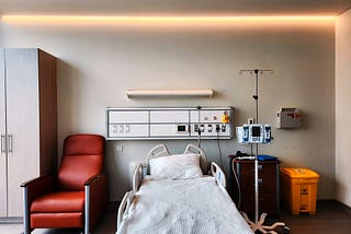 A picture of an empty hospital bed and an empty seat next to it.