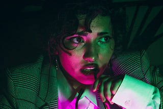 anxious-looking woman wearing a business suit in a dimly lit room