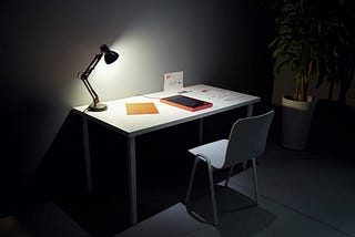 Lamp shining down on desk in a low lit room