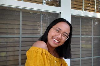 A girl in a yellow top smiles while sitting outside.