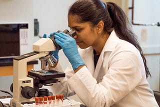 Woman in white lab coat looking into a microscope
