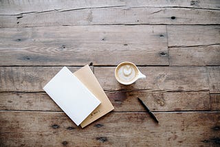 A blank sheet of paper sits next to a pen and coffee with love heart showing through froth.