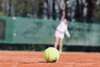 Tennis player hitting a tennis ball with a racket with a visual of another tennis ball up front