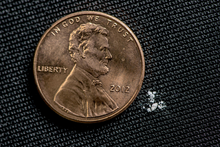 A small amount of white fentanyl is shown next to a much larger penny.