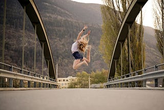 woman jumping up in the air on a bridge