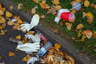 Trash lying on the ground, plastic bottles, cups, used gloves lying in street