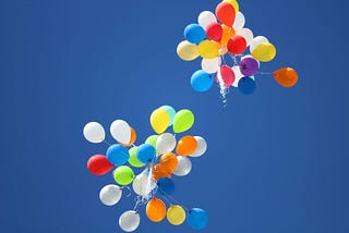 Two bunches of colorful balloons floating in a blue sky.