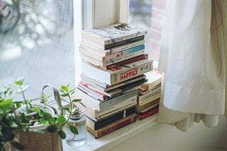 stack of books on sunny windowsill next to a plant