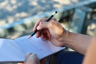 a hand sketching a building outside under mottled light