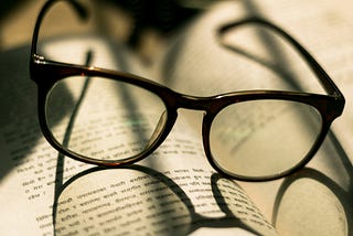 A pair of glasses cast a shadow on the text of a book.