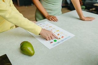 A person explaining a food chart to another individual and a pear kept on a table by the side.