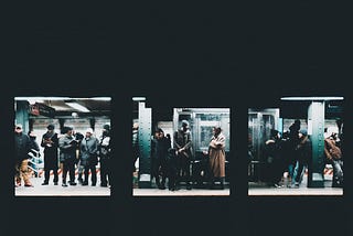 A group of people stand in a subway awaiting a train