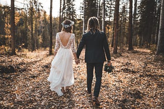 A couple in wedding outfits walk hand in hand into forest after exchanging their pagan wedding vows.