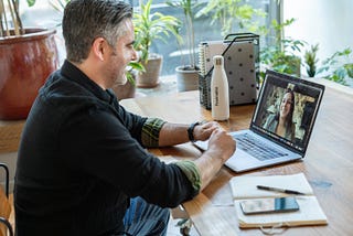 Man on a video chat sat at a desk with his laptop