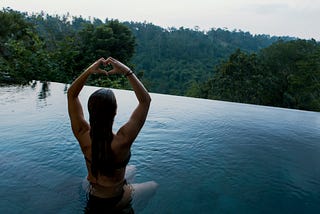 A woman in a swimming with her hands up and her finger folded into a love symbol