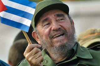 Fidel Castro in close-up, in military fatigues, laughing, and waving a small Cuban flag