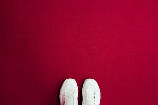 A pair of visible white trainers on a red carpeted background