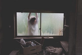 Ethereal figure outside and pressed against wet glass window of storage shed